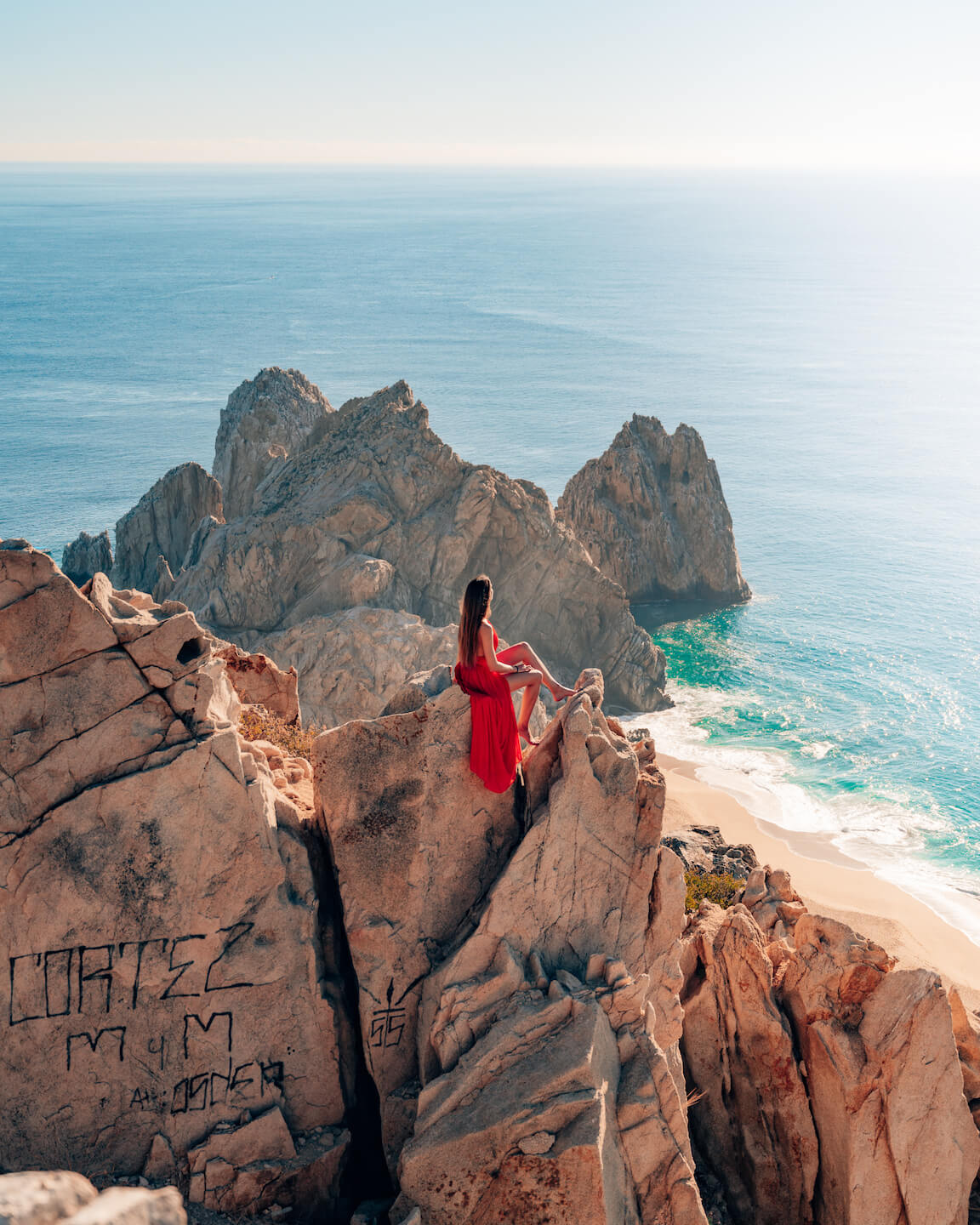 girl in red dress sitting on a rock in cabo san lucas