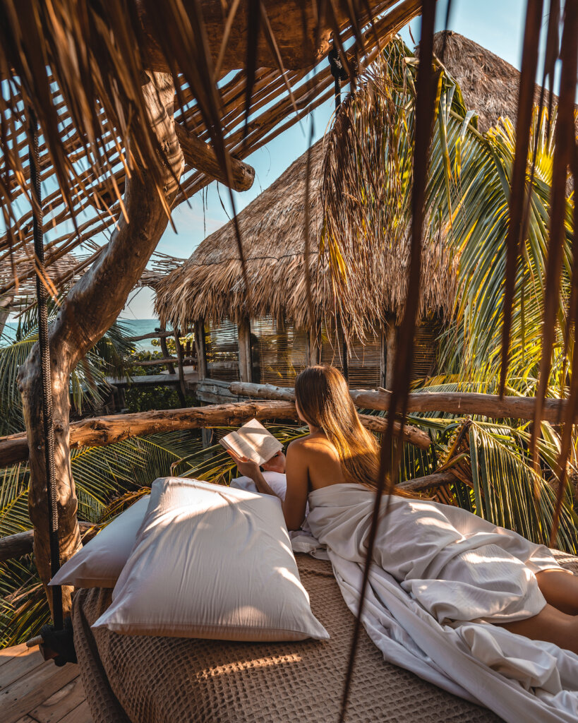 girl laying on mattress in the jungle reading a book and watching the ocean in Tulum